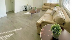 Amplia sala de estar con un sofá color beige, una mesa de centro y un televisor montado en la pared.