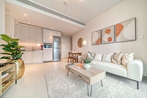 A modern living room with a white sofa, a wooden coffee table, and a dining area with a table and chairs. - Marina View w/ Beach Access Apt in Address JBR (Dubai)