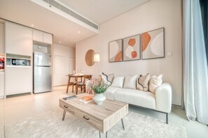 A modern living room with a white sofa, a wooden coffee table with a vase, abstract wall art, and a dining area with a table and chairs.