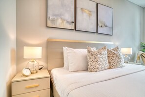 A neatly arranged hotel room with a bed, bedside lamps, a nightstand with a clock, and abstract wall art. - Marina View w/ Beach Access Apt in Address JBR (Dubai)