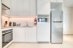 A modern kitchen with white cabinetry, a stainless steel refrigerator, an oven, and a microwave.