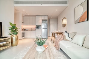 A modern living room with a sofa, a coffee table with a plant, a dining area with a table and chairs, and a kitchen with cabinets and appliances.