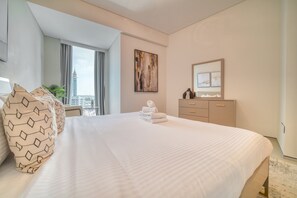 Habitación de hotel con una cama grande, un escritorio, una silla, un ventanal con vista a un paisaje urbano y un cuadro en la pared.