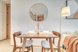 Ein Essbereich mit einem Holztisch, gedeckt für zwei Personen, einem runden Spiegel darüber und einer Lampe zur rechten Seite.