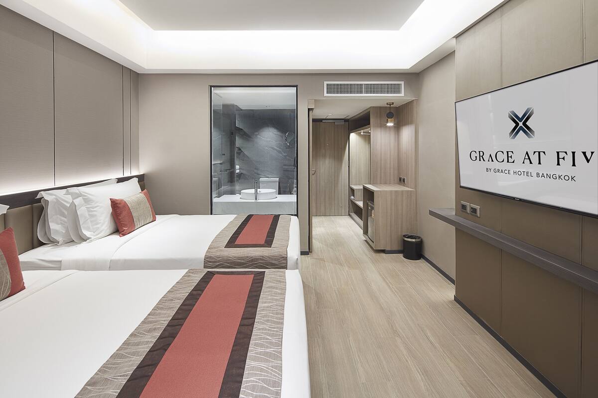 A modern hotel room with two beds, a large mirror, and a view of the bathroom.