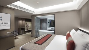 A modern hotel room with a large bed, a bathroom with a bathtub, a shower, and a vanity. There is a desk with a chair and a large window.
