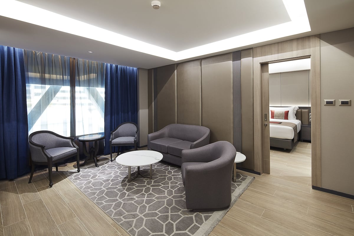A modern hotel room with a sofa, chairs, a small table, and a bed.