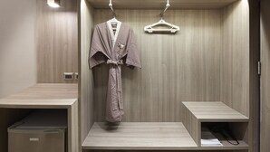 A modern bathroom with wooden paneling, a robe hanging on a rack, and a small shelf with a towel.