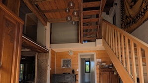 Un intérieur en bois avec un escalier, une cheminée et un couloir menant à une autre pièce.