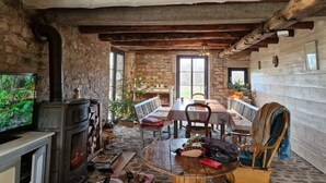 Un intérieur rustique avec une cheminée en pierre, des poutres en bois, une table à manger avec des chaises et un téléviseur.