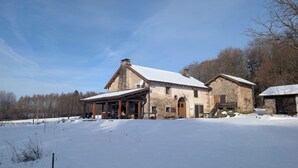 Un edificio de piedra con techo nevado, un porche cubierto y una estructura pequeña contigua.