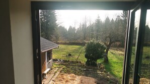 Une fenêtre donnant sur un jardin, avec notamment un mur en pierre et une structure en bois.