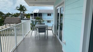 A balcony with a table and chairs, a ceiling fan, and a view of the ocean and other buildings. - Great House in Key Largo (Key Largo)