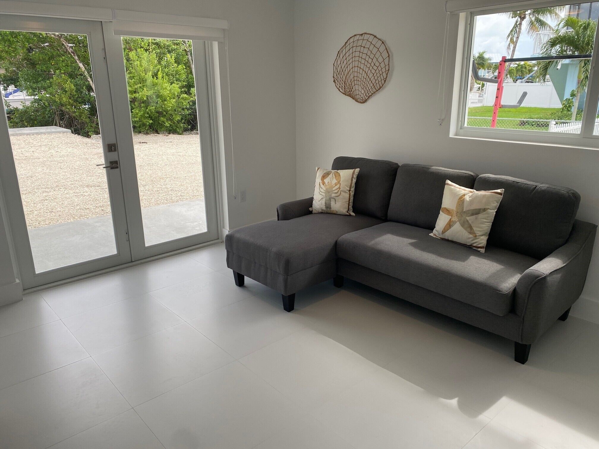 A modern living room with a grey sectional sofa, two decorative pillows, a round wall hanging, and a large sliding glass door leading to a patio area.