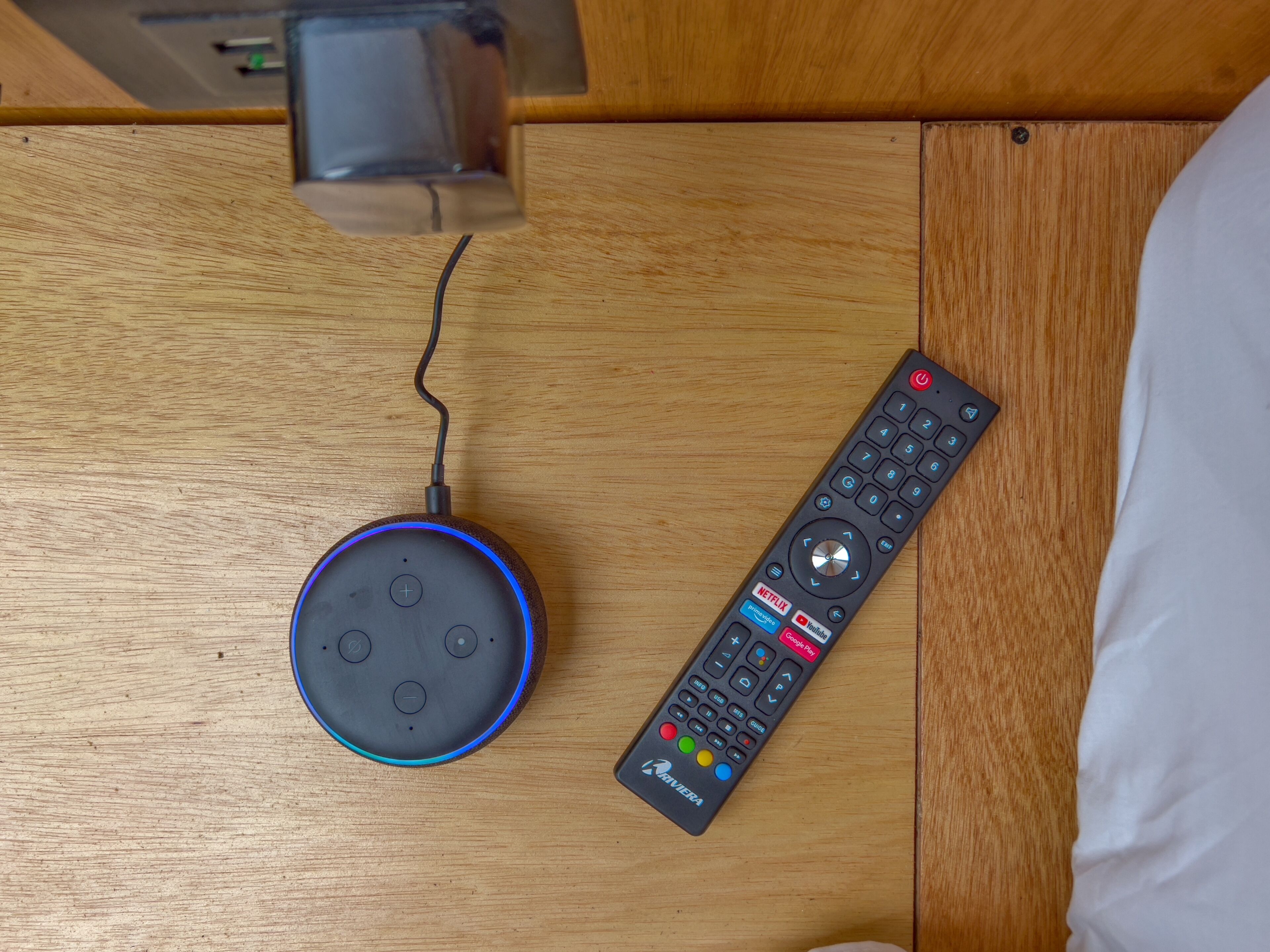 Una cama con sábana blanca, cabecero de madera y un control remoto sobre una superficie de madera.