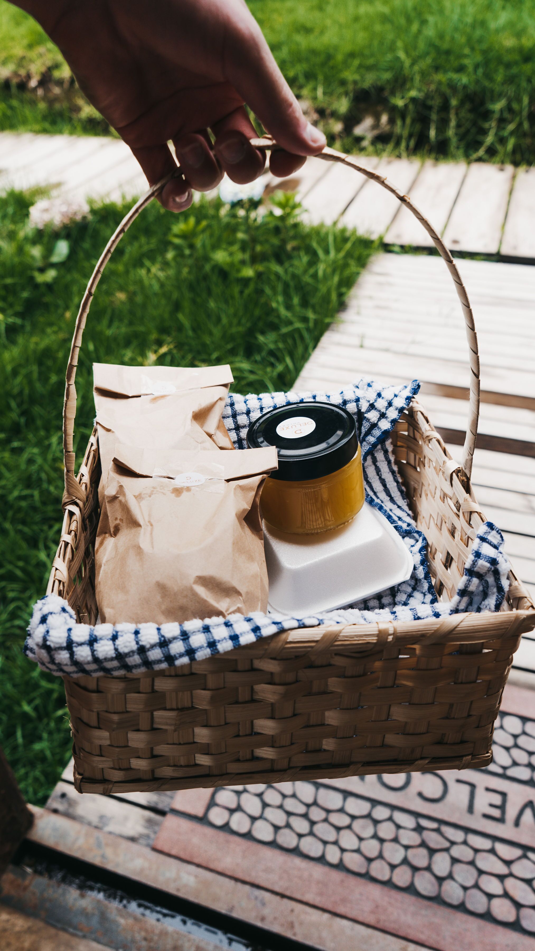 Una cesta de mimbre con una botella y una bolsa de papel sobre una cubierta de madera.