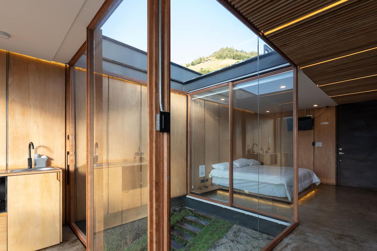 Une chambre moderne avec une cloison en verre, des meubles en bois, un lit et une petite kitchenette.