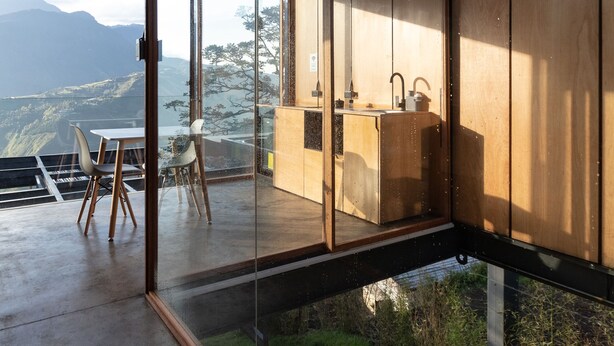 A modern interior with large glass windows, a wooden ceiling, and a view of a mountainous landscape.