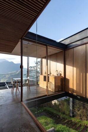 A modern interior with large glass windows, a wooden ceiling, and a view of a mountainous landscape. - Deluxe Volcán (Baños de Agua Santa)