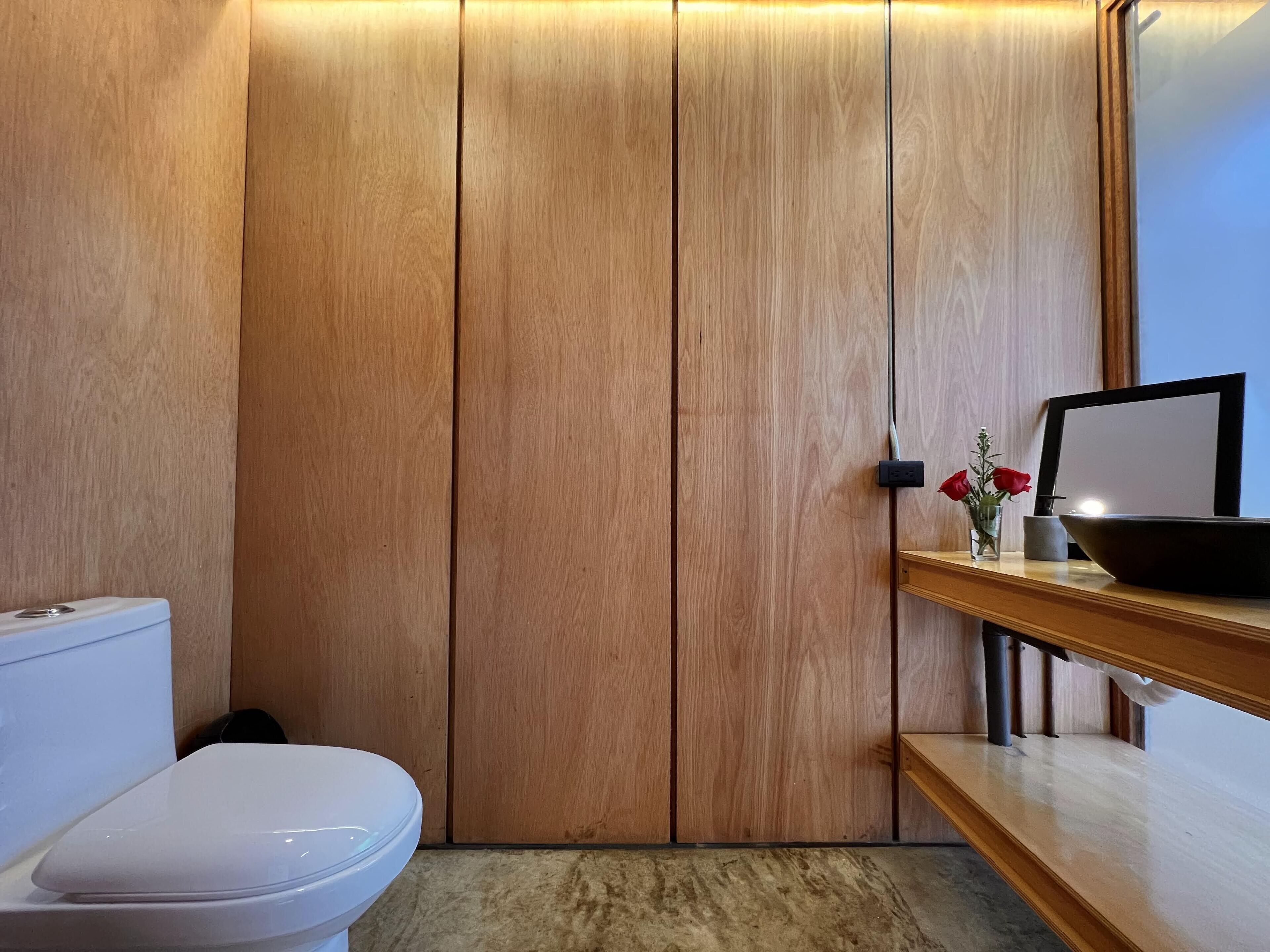A modern bathroom with a wooden vanity, a white toilet, and a mirror.