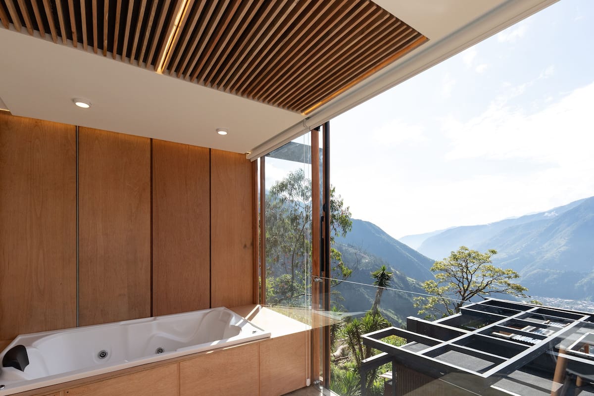 Une salle de bain moderne avec une grande baignoire, un lambris en bois et une vue sur les montagnes grâce à de grandes fenêtres.