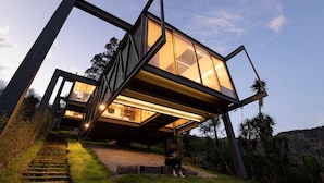 A modern house with a glass facade, a staircase leading to the entrance, and a view of the surrounding landscape.