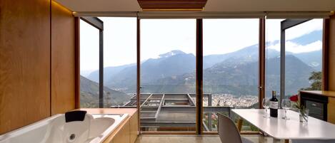 A modern bathroom with a large bathtub, a sink, and a table with a rose and wine bottle.