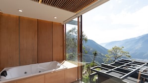 A modern bathroom with a large bathtub, wooden paneling, and a view of mountains through large windows.
