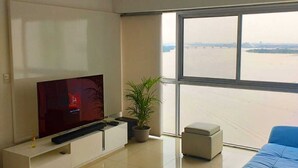 A modern living room with a large TV, a potted plant, and a blue sofa. - Departamento Emporium  (Guayaquil)