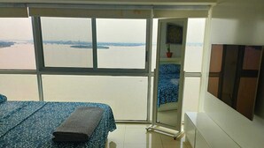 A room with a bed, a TV, and a view of a body of water through large windows. - Departamento Emporium  (Guayaquil)