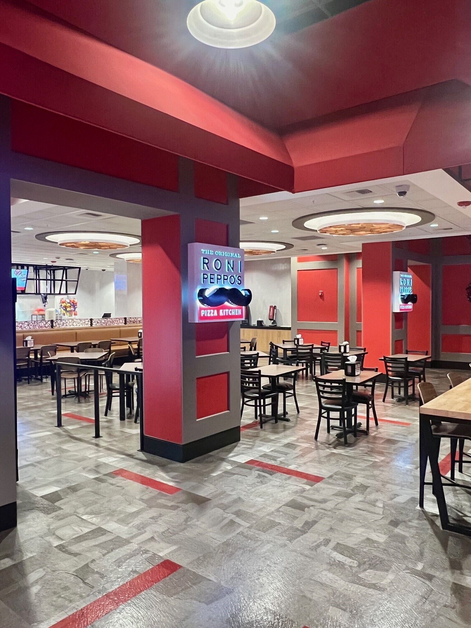 Un interior de restaurante con paredes rojas, varias mesas y sillas, y un letrero de neón para Roni Peppo's Pizza Kitchen.