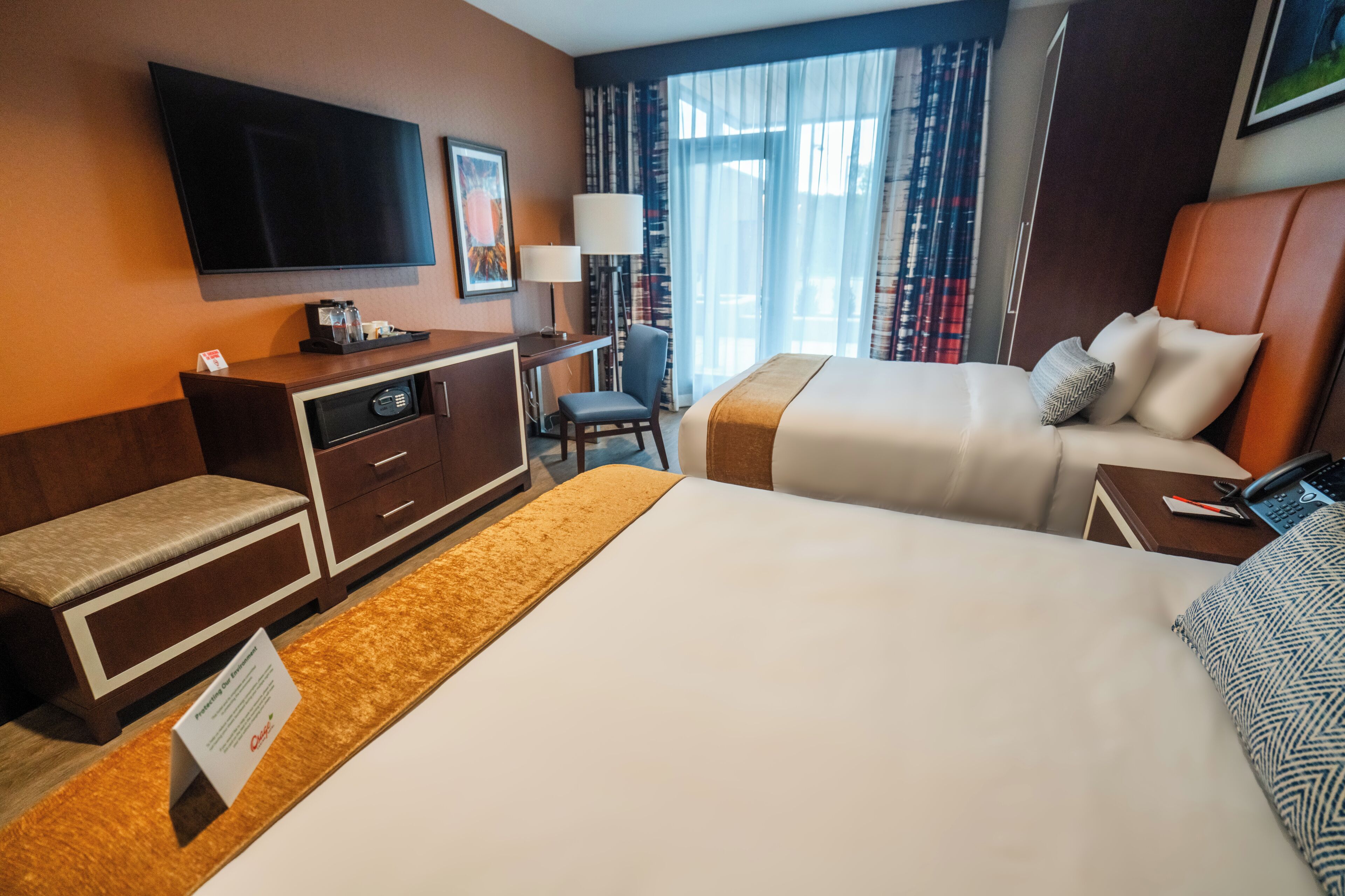 A hotel room with a large bed, a desk with a chair, a television mounted on the wall, and a window with curtains.
