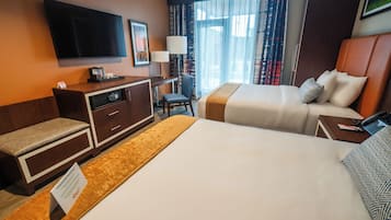 A hotel room with a large bed, a desk with a chair, a television mounted on the wall, and a window with curtains.