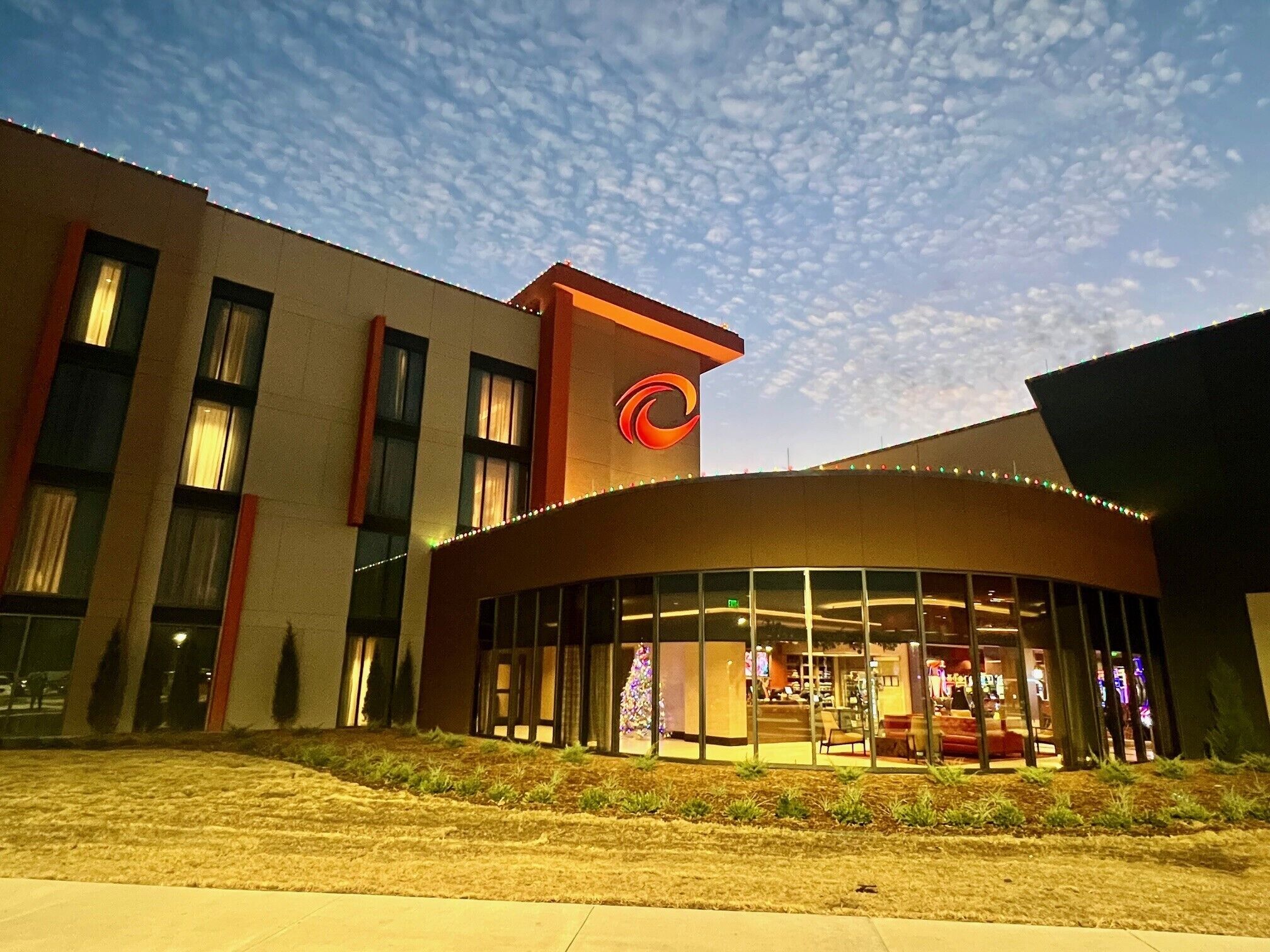 A modern building with a curved glass entrance and a prominent red logo on the facade.