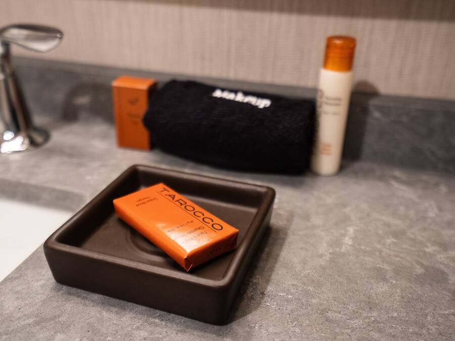 Una encimera de baño con una caja de artículos de aseo, una toalla negra y una botella de champú.