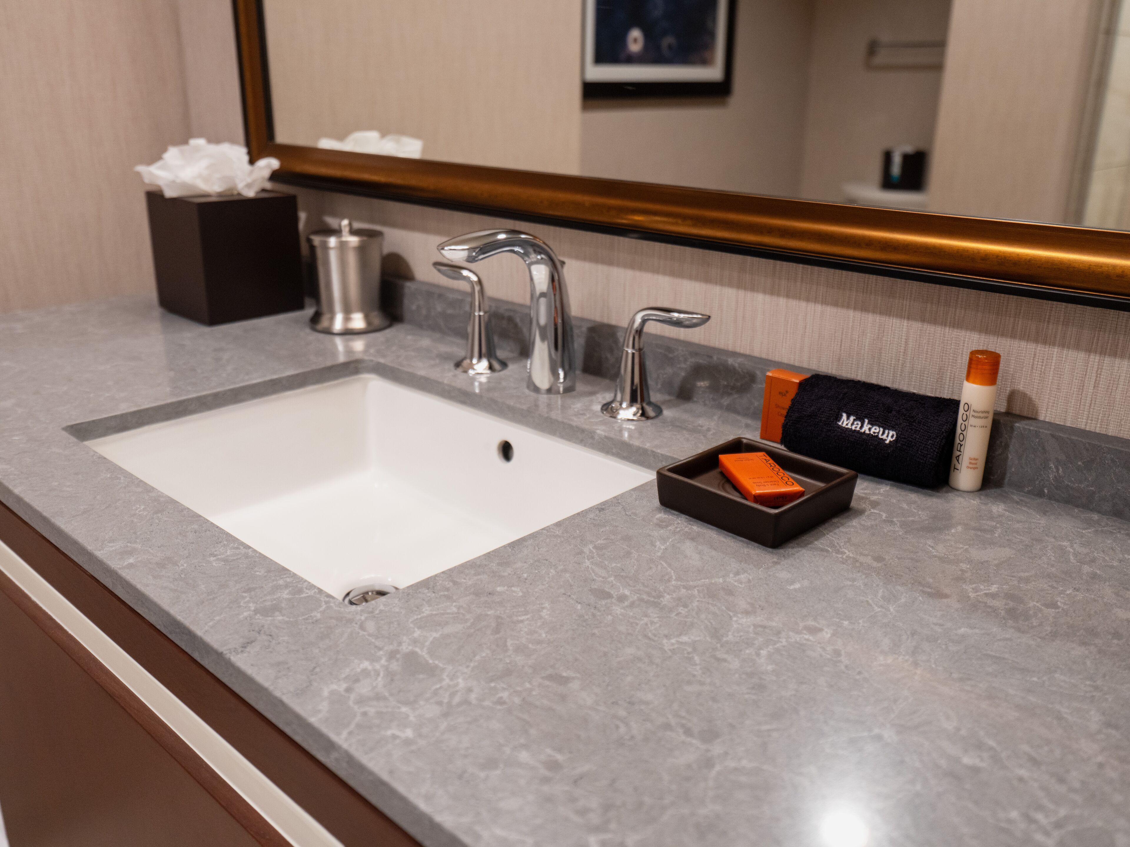 A bathroom sink with a mirror above it, a tissue box, a makeup item, and a bottle of hand soap.