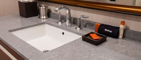 A bathroom sink with a mirror above it, a tissue box, a makeup item, and a bottle of hand soap.