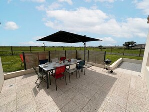 Um pátio externo com mesa, cadeiras, churrasqueira e vista para um campo.