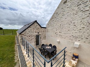 A stone building with a small balcony, a table with chairs, and a view of the countryside.