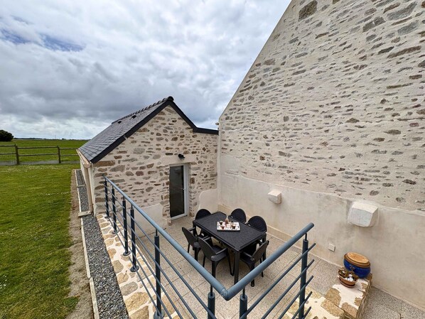 A stone building with a small balcony, a table with chairs, and a view of the countryside.