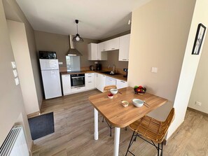 A modern kitchen with white cabinets, a built-in oven, a coffee maker, and a dining table with two chairs.