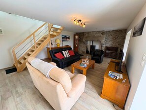 Uma sala de estar com escada de madeira, um sofá de couro preto, um sofá bege, uma mesa de centro de madeira e uma lareira de pedra.