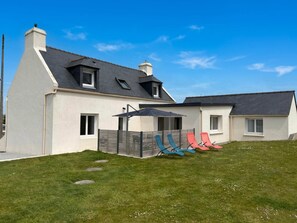 Une maison à deux étages avec un toit en pente, une cour arrière clôturée et un patio aménagé avec du mobilier d’extérieur.