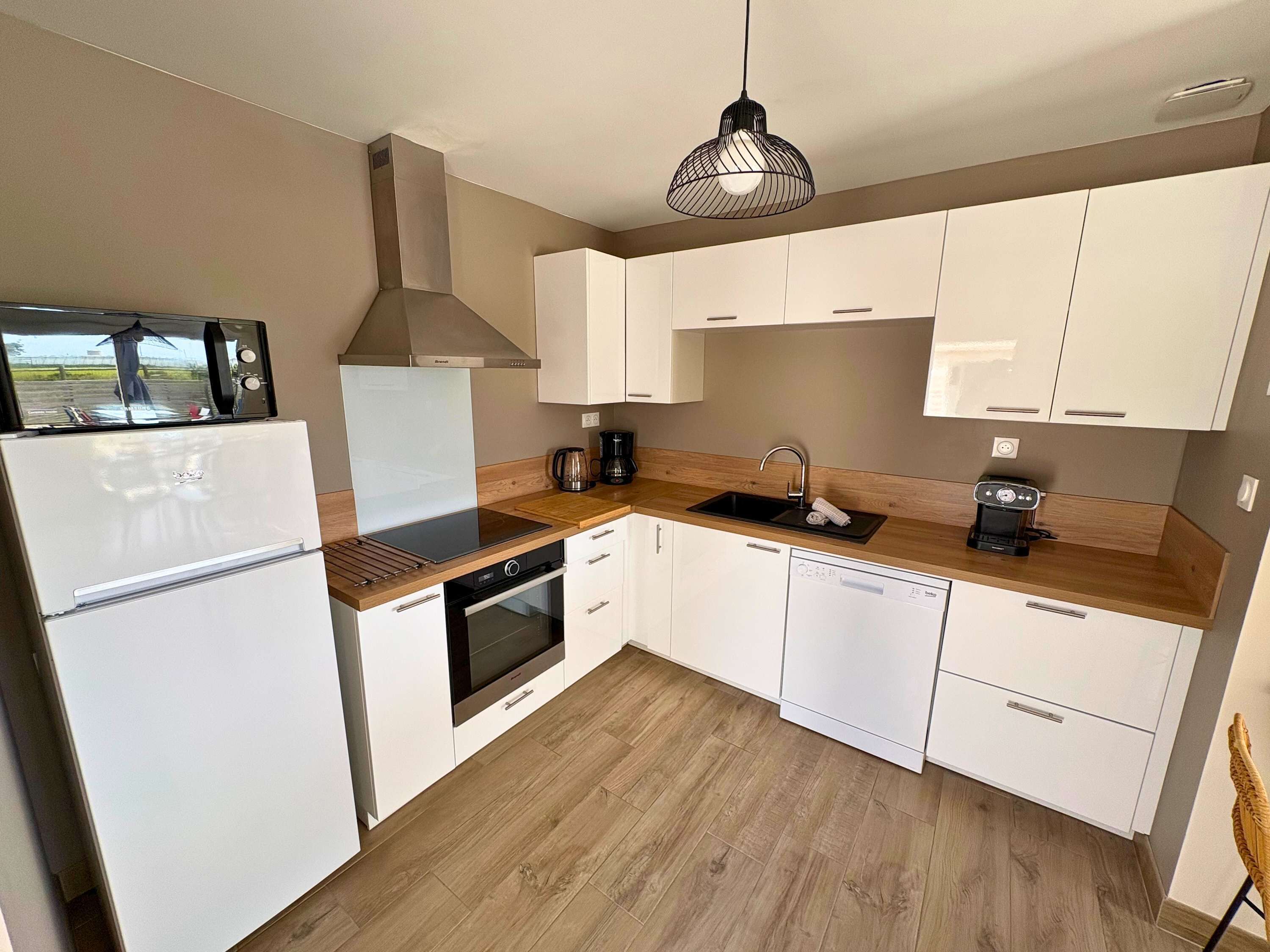 A modern kitchen with white cabinets, a built-in oven, a coffee maker, and a hanging light fixture.