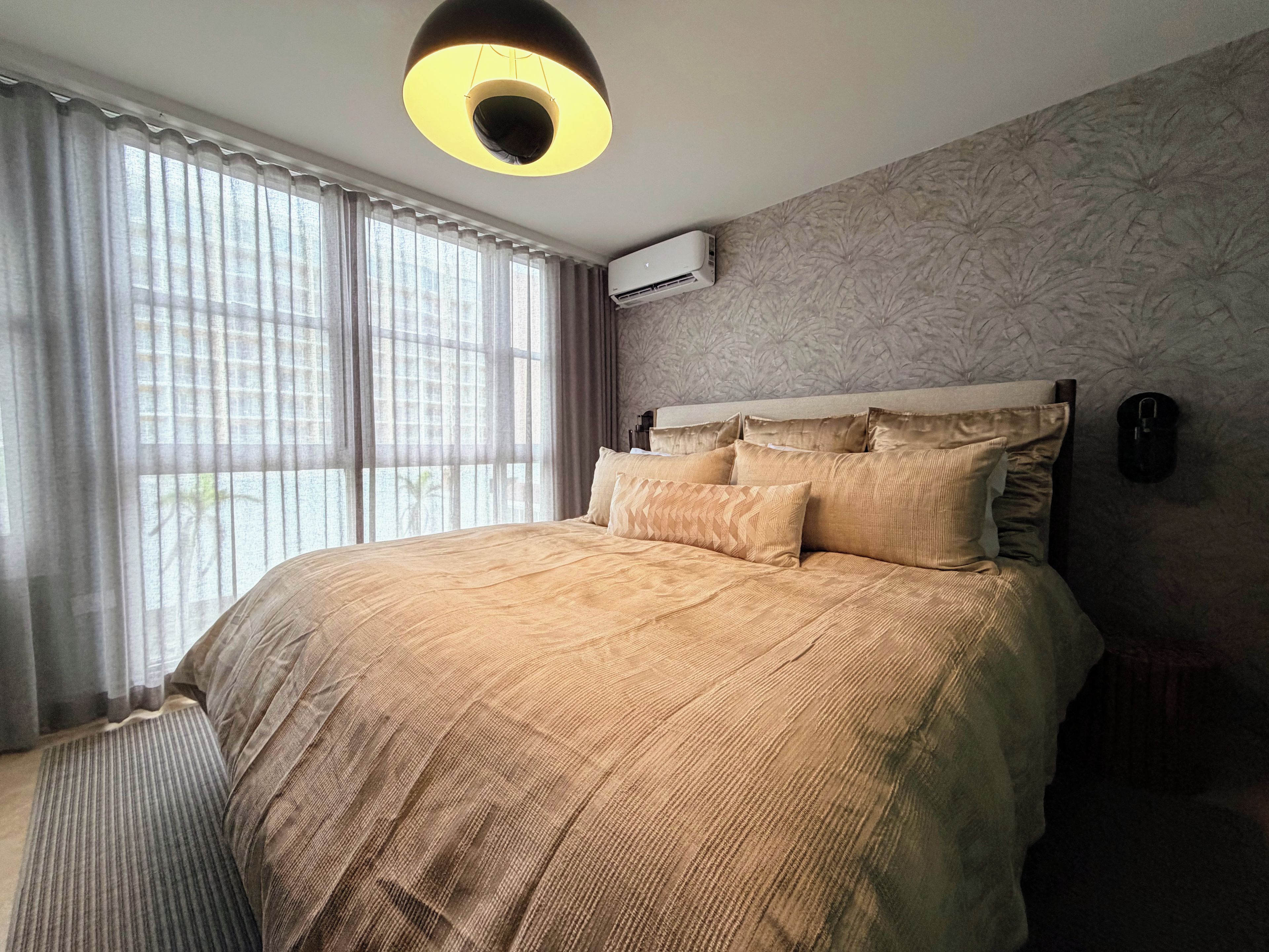Una camera da letto con un letto grande, un lampadario, un condizionatore e una finestra con tende.