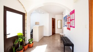 Un couloir comprenant un comptoir d’accueil, des plantes en pot, un banc et un panneau d’affichage où sont accrochées des annonces.