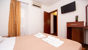 Une chambre d’hôtel avec un lit, une télévision, un bureau agrémenté d’une plante et une porte donnant sur une autre pièce.