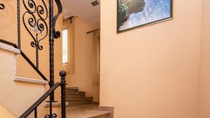 Un escalier orné d’une rampe en fer forgé, un tableau encadré au mur et un luminaire au-dessus.