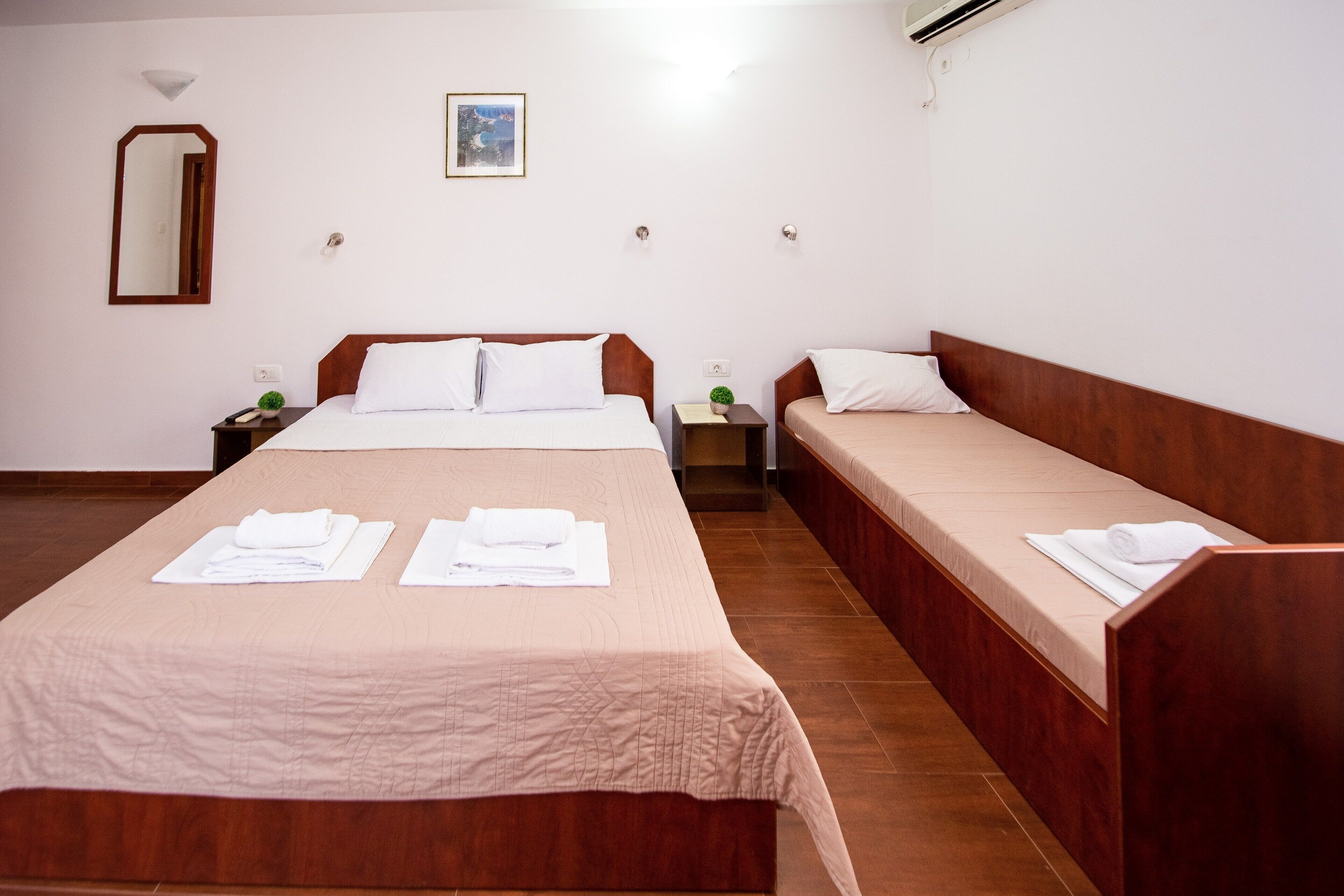 A hotel room with two beds, a large mirror, a small plant, and a painting on the wall.