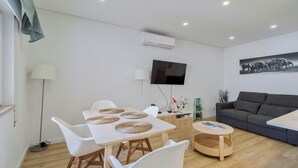 A modern living room with a dining area, a grey sofa, a flat-screen TV, and a painting on the wall. - Fonte Nova Nest (Sesimbra)